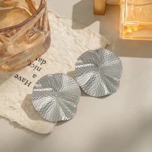 Macro view of silver ruffled wavy stud earrings with hammered texture on a paper background