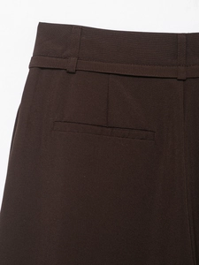 Dettaglio dei pantaloni larghi marrone scuro che mostra i passanti e la tasca a filetto