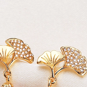 Elegant gold ginkgo leaf earrings with white zircon accents on white silk fabric
