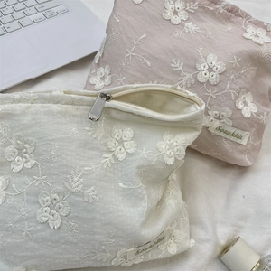 Close-up of floral embroidery on cream and pink cosmetic bags with metal zippers