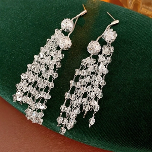 Close-up of silver tassel earrings with transparent crystals on dark green velvet fabric