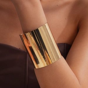Breite polierte Goldmanschetten-Armspange am Handgelenk eines Models, minimalistisch