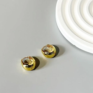 Detail view of chunky golden water drop hoop earrings on a minimalist grey background