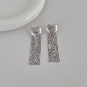 Detailed close-up of silver heart-shaped brushed metal earrings with long elegant tassels