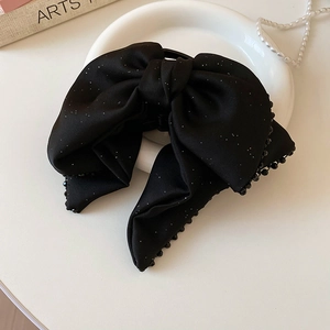 Detail of black bow hair claw with glitter finish and beaded edges on white plate