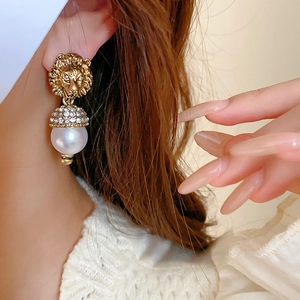 Close-up of golden lion head earring with crystal sphere and white pearl on model