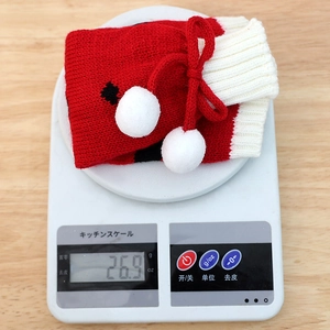 Knitted Christmas wine bottle cover in red and white with plush balls and bow decoration