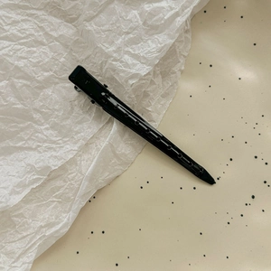 Detail of glossy black metal hair clip with non-slip handle for professional hair styling