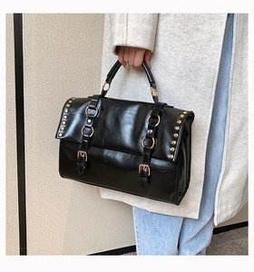 Detail of vintage black satchel bag with golden rivets and metallic ring accents