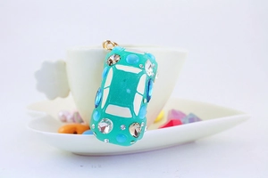 Detail of green car keychain with colorful rhinestones on a white ceramic tea cup
