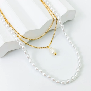 Detailed close-up of layered gold chains and white pearls on a minimalist stone background