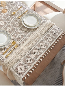 Detail of beige lace crochet tablecloth featuring geometric patterns and fringe edges