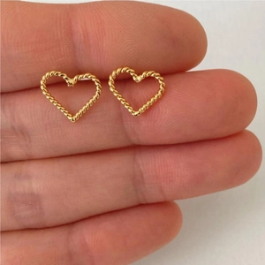Detail of hand holding a golden heart-shaped twist earrings with textured rope design