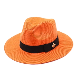 Detail of orange straw Panama hat with black ribbon and gold bee metal buckle