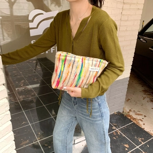 Outdoor street style view of a colorful striped knit pouch held by a model
