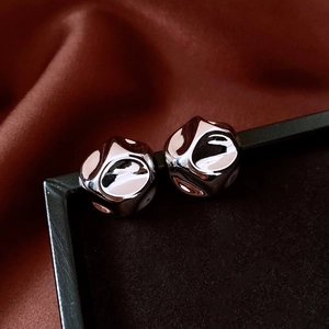 Detailed close-up of silver-toned liquid metal stud earrings on silk background
