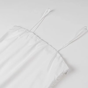 Detail of white camisole dress featuring thin straps and textured pleated fabric design