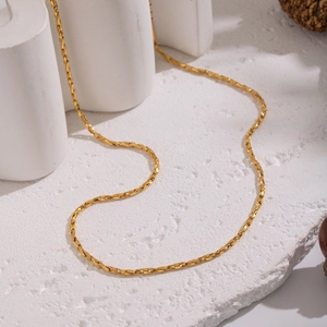 Gold stainless steel flat twist chain necklace on white stone display minimalist style
