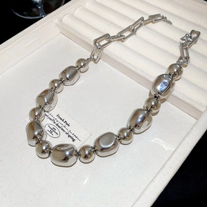 Détail d'un collier à billes argentées irrégulières sur velours avec maillons rectangulaires
