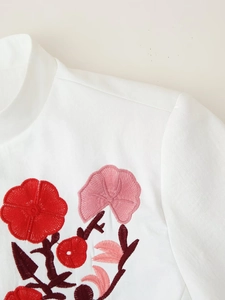 Close-up of floral embroidery in shades of red on the lapel of a white blazer jacket