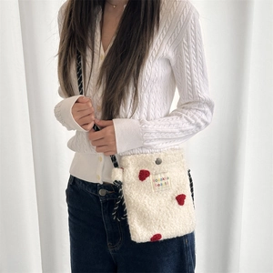 Detail of white plush crossbody bag featuring red heart embroidery and woven brand label