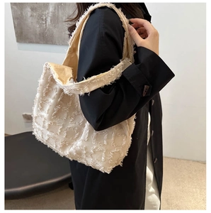 Close-up of beige plaid tote bag with fringe details styled on a black coat outfit