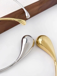Detailed close-up of metallic teardrop neck ring in polished gold and silver finishes