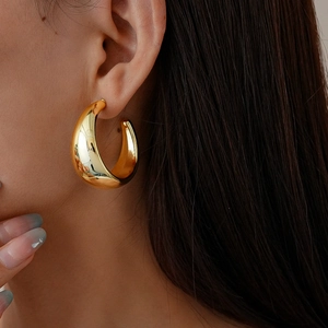 Close-up of a model wearing a thick, polished gold geometric C-shaped hoop earring