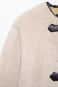 Détail de la texture en fausse fourrure crème avec bordure en cuir marron et bouton corne