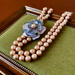 Detailed macro view of vintage lavender enamel flower pendant on a double pearl necklace