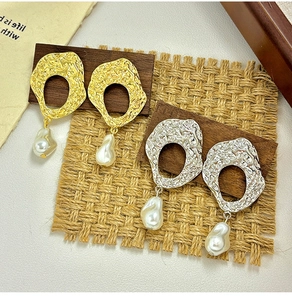 Detail view of baroque pearl earrings with hammered metal rings on a wooden stand