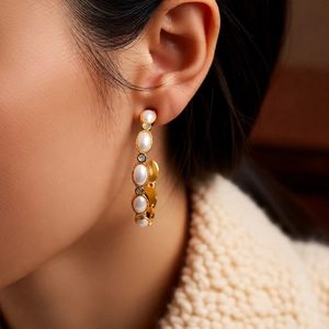 Detailed close-up of C-shaped gold-plated hoop earrings with pearls and crystals on ear