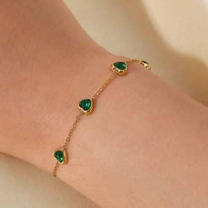 Bracelet cœur doré avec des pierres en zircon vert sur un tissu en soie brillante