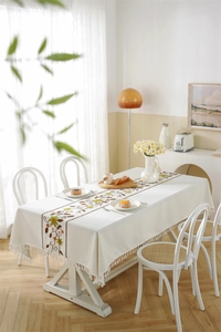 Detail of beige linen rectangular tablecloth featuring floral embroidery and tassels
