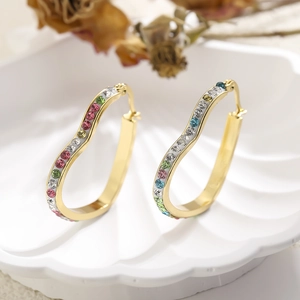Macro detail of gold heart hoop earrings with colorful crystals on a shell tray
