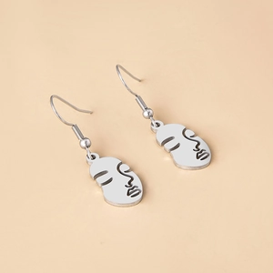 Macro detail of abstract silver face earrings with minimalist hollow line art design