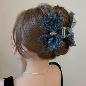 Detail view of a black polka dot mesh bow hair claw with rhinestones on dark brown hair