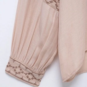 Close-up of beige long sleeve shirt cuff with elegant floral embroidery and pleated design
