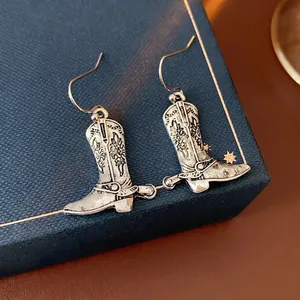 Vintage silver cowboy boot earrings with floral engraving and spur details on a box