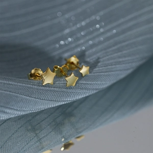 Macro shot of gold star-shaped stud earrings on soft textured fabric with a butterfly clasp