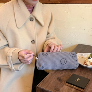 Detail of grey corduroy cosmetic bag with embroidered smiles on a wooden cafe table