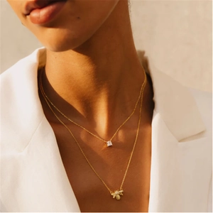 Close-up of golden layered necklace with a square gemstone and honey bee pendant