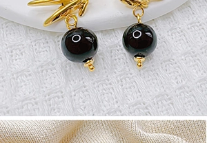 Gros plan d'un pendentif en métal doré avec une perle noire sur un tissu texturé blanc