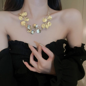 Close-up of a gold leaf statement necklace worn by a model in a stylish off-shoulder outfit