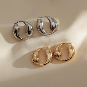 Detail view of gold and silver fluid loop earrings on a soft beige satin background
