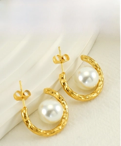 Détail de boucles d'oreilles C en métal martelé doré avec perles rondes blanches