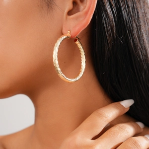 Close-up of golden geometric twisted rope hoop earrings worn on a model's ear