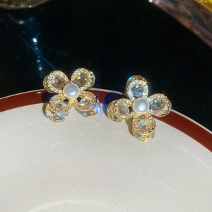 Détail de boucles d'oreilles fleur dorées avec perle et zircone sur une assiette