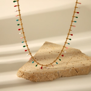 Detail of gold necklace with colorful enamel charms on a textured stone display