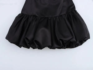 Detail of black satin mini skirt showing smooth fabric and puffy bubble hemline